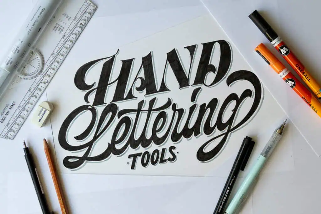 Hand lettering tools and materials on a workspace.