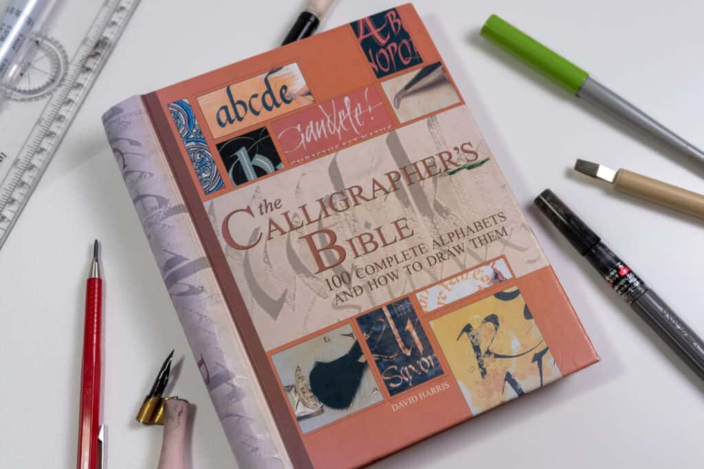 Cover image of the Calligrapher's Bible book with calligraphy pens around it.