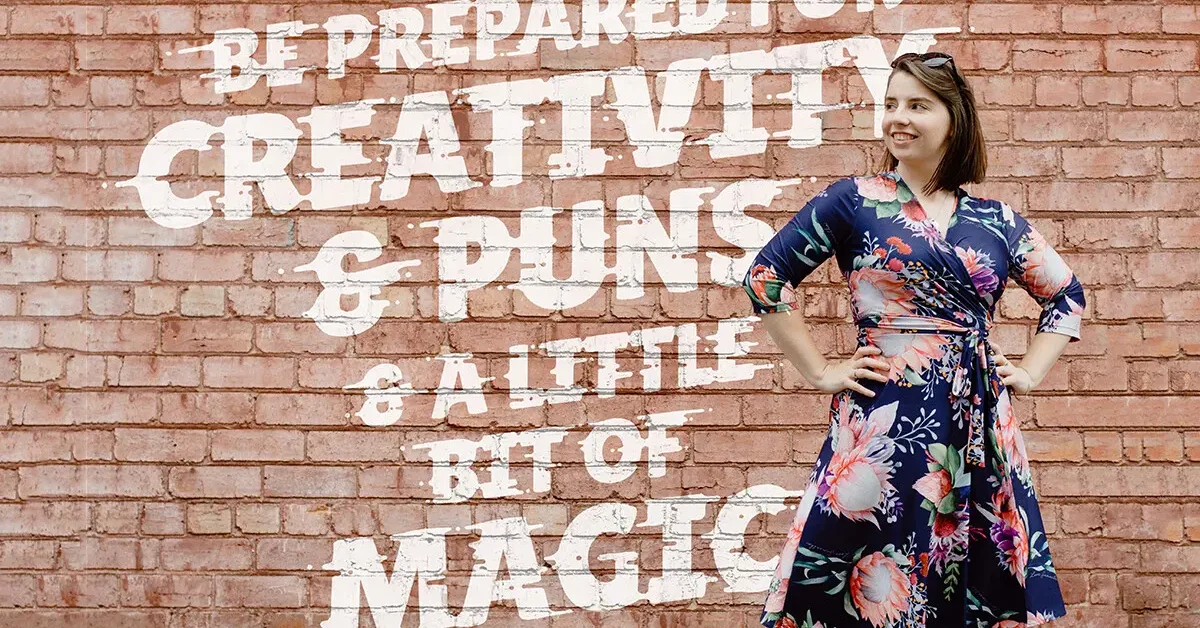 Woman in floral dress posing against brick wall.