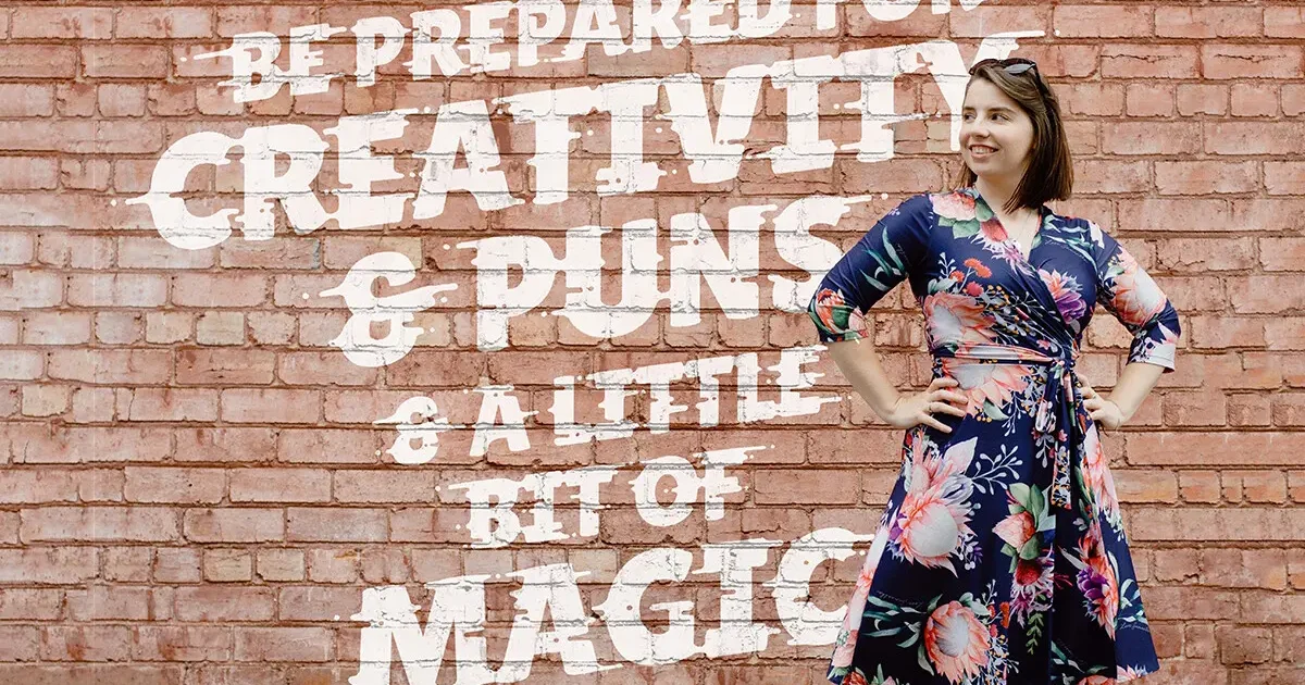 Woman in floral dress posing against brick wall.