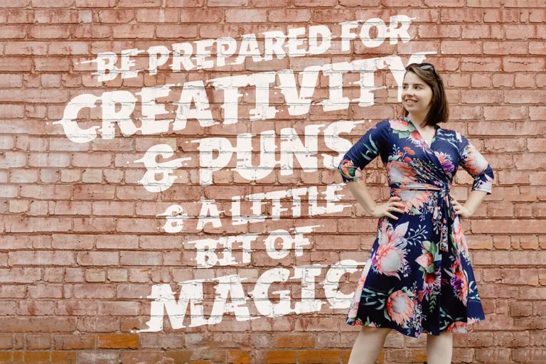Woman in floral dress posing against brick wall.