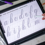 Hand tracing lowercase letters on a digital tablet.