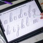 Hand tracing lowercase letters on a digital tablet.