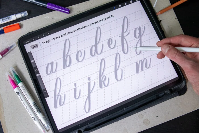 Hand tracing lowercase letters on a digital tablet.