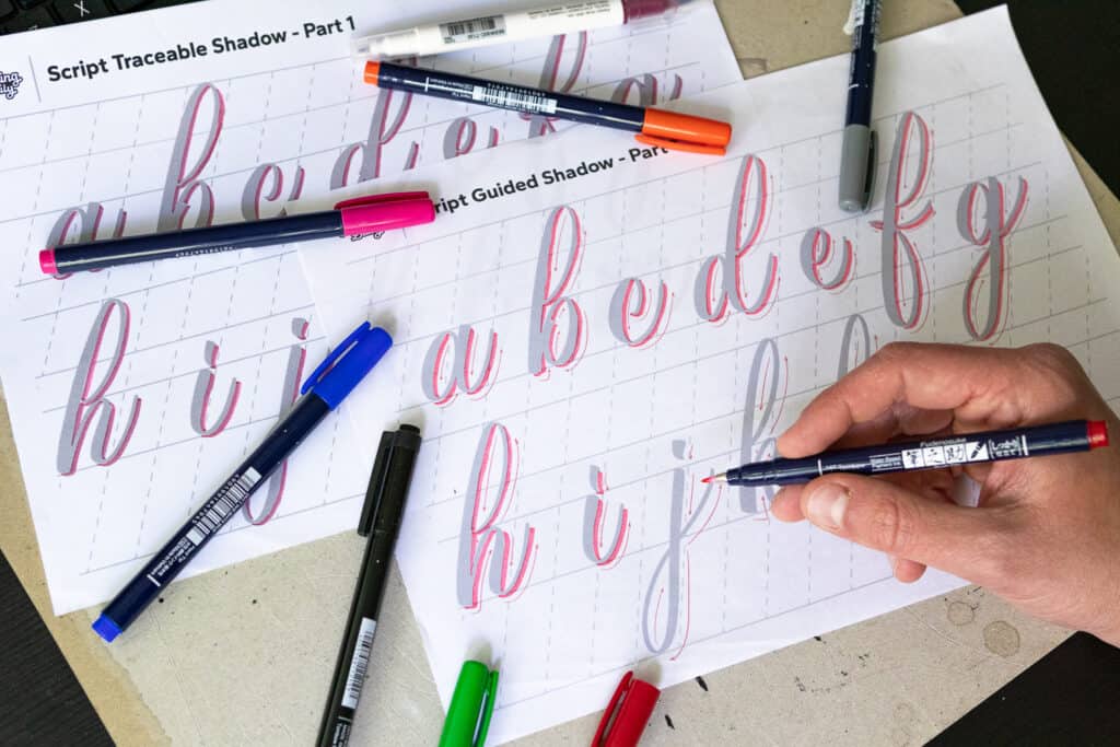 Hand illustrating letters with colorful markers.
