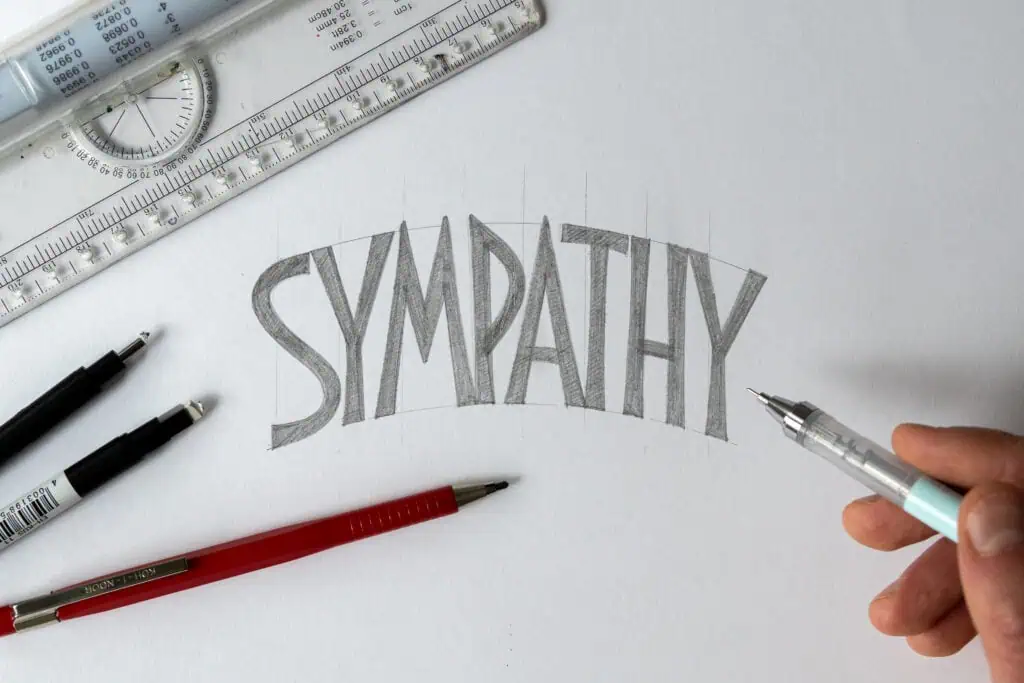 Hand sketching the word 'SYMPATHY' on paper.